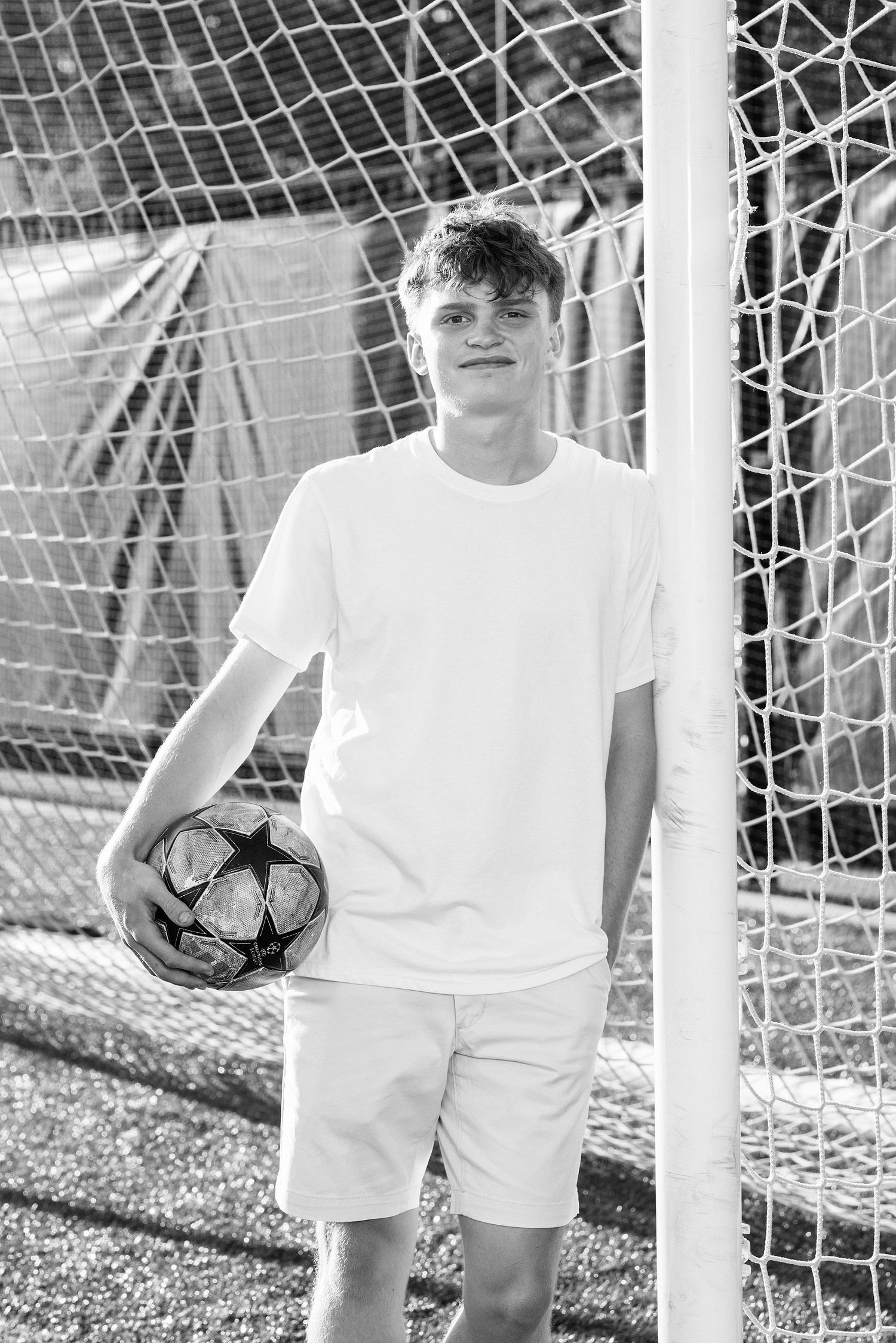 A soccer player holds a ball while standing next to a goal post with netting visible.
