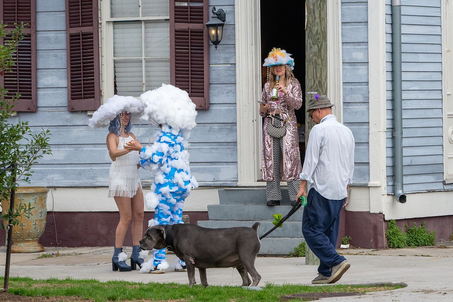 People in costumes gather on a house porch with a decorative dog statue.