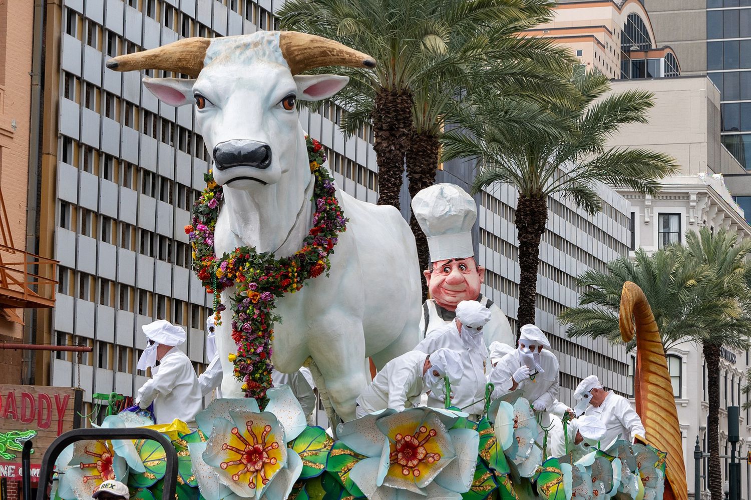 White bunny-themed Mardi Gras parade float with floral decorations against palm trees and buildings.