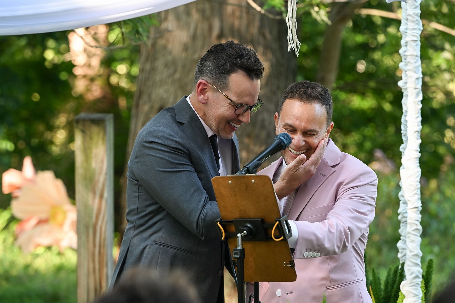 Two people share an emotional moment while looking at a wooden box during an outdoor ceremony under a gazebo.
