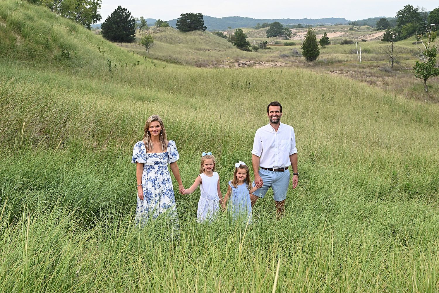 A family stands together in a grassy field with rolling hills in the background.