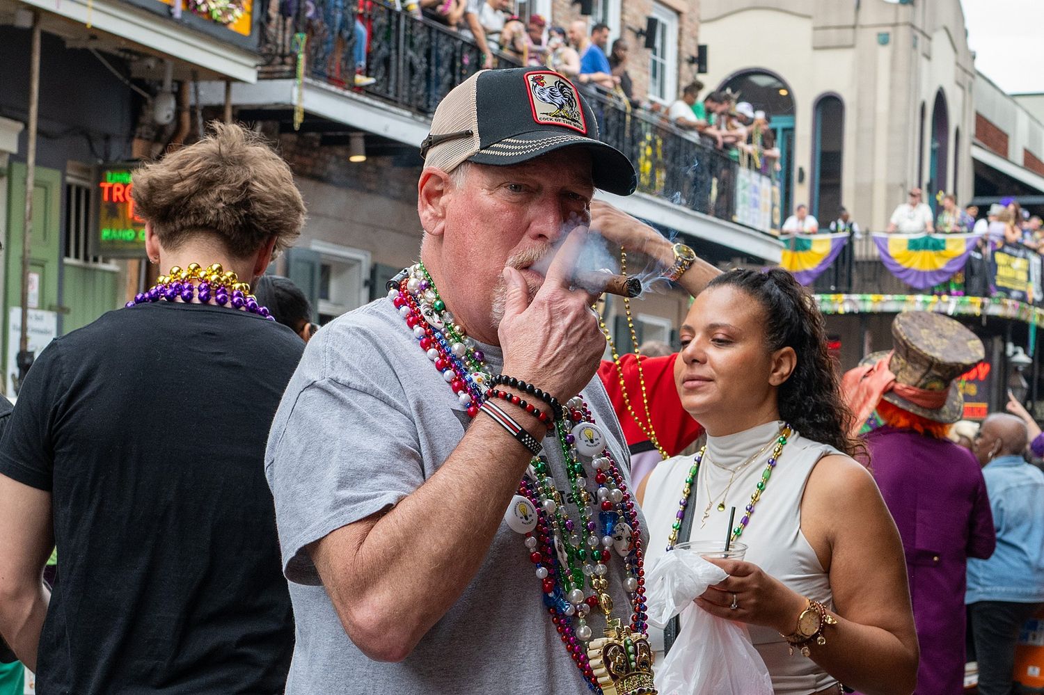 Crowded street celebration during Mardi Gras with revelers wearing festive attire and beads.