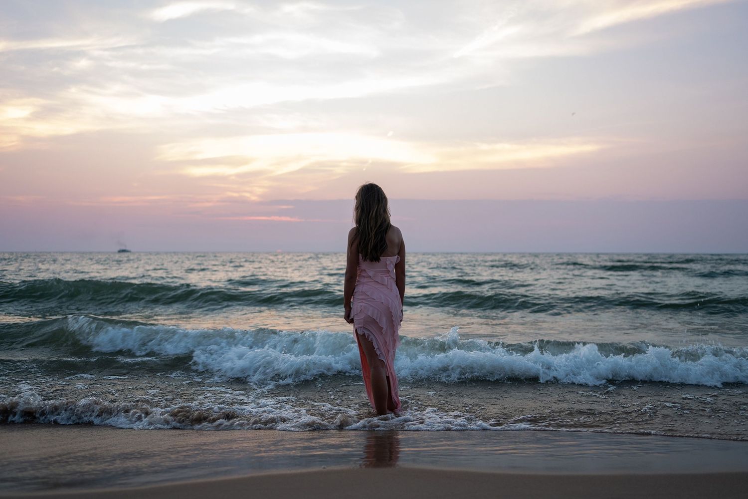 Waves rolling onto beach at dusk with warm sunset colors in the sky.