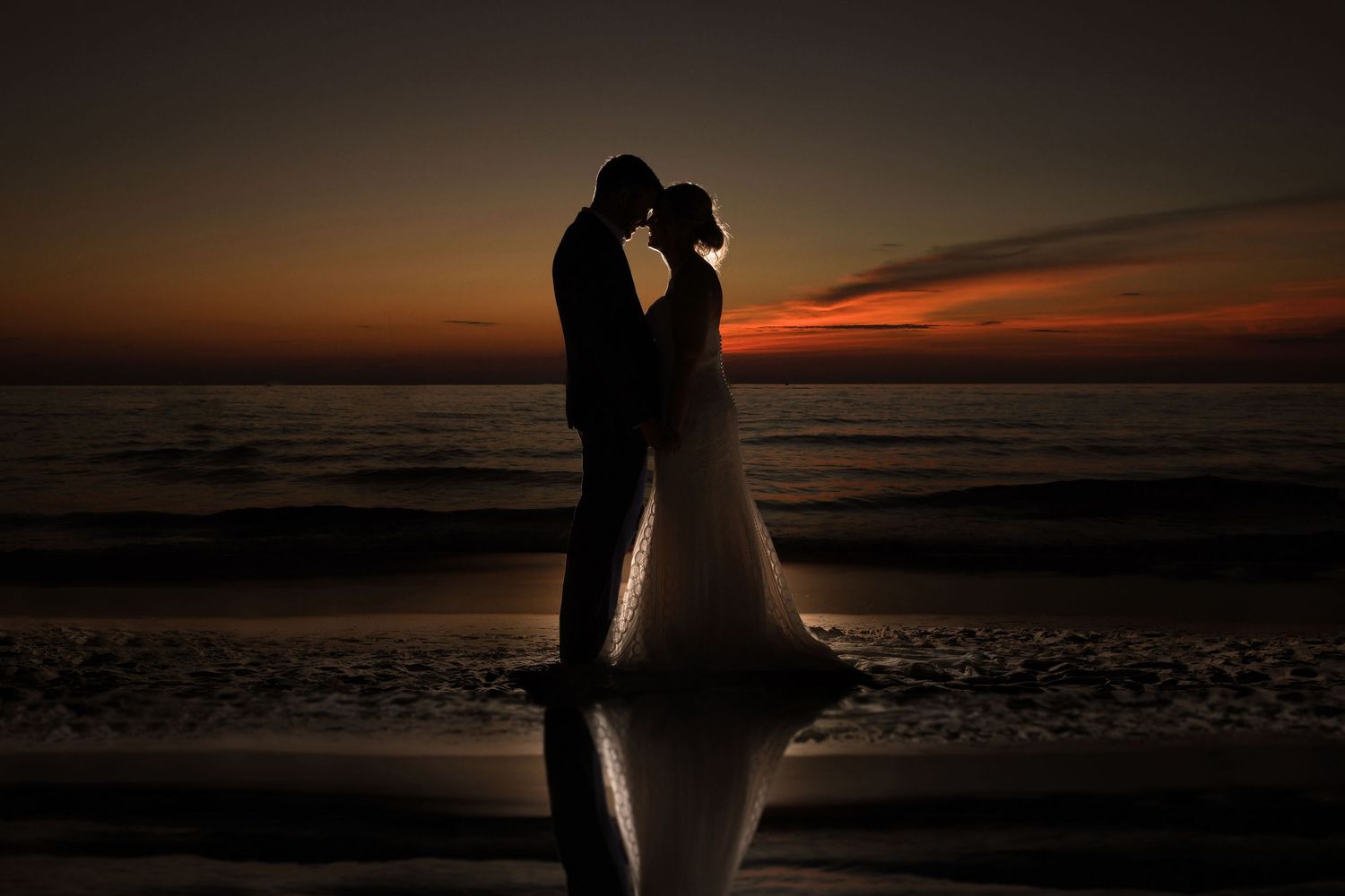 Silhouettes of romantic couple against dramatic sunset on beach.