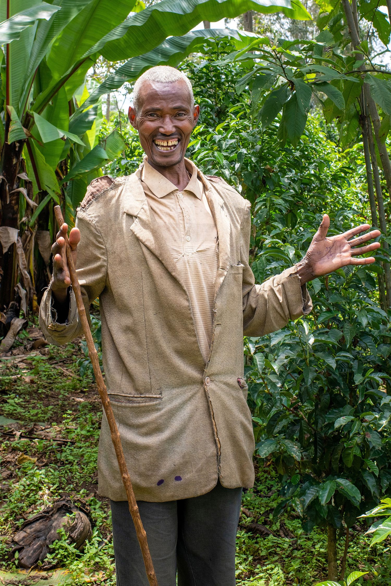 An elderly person in beige clothing gesturing expressively in a lush garden setting.