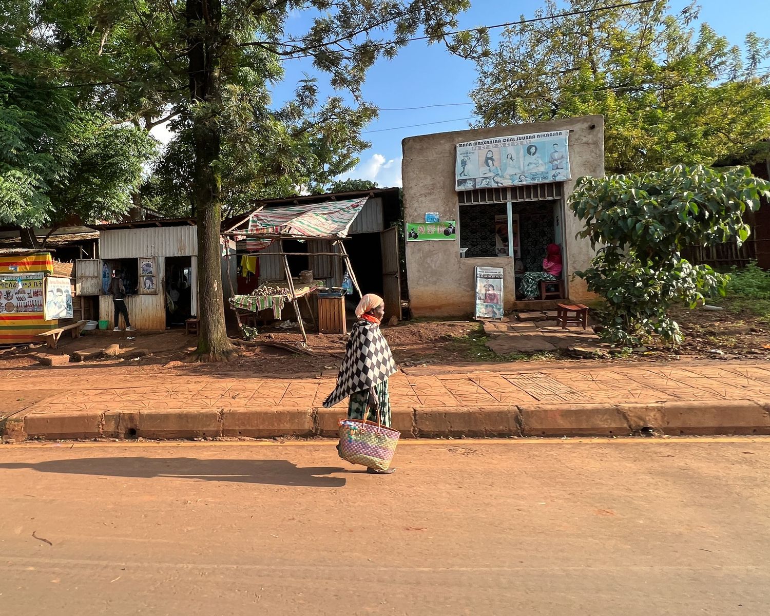 Row of small shops and buildings along a dusty red dirt road in a rural village.