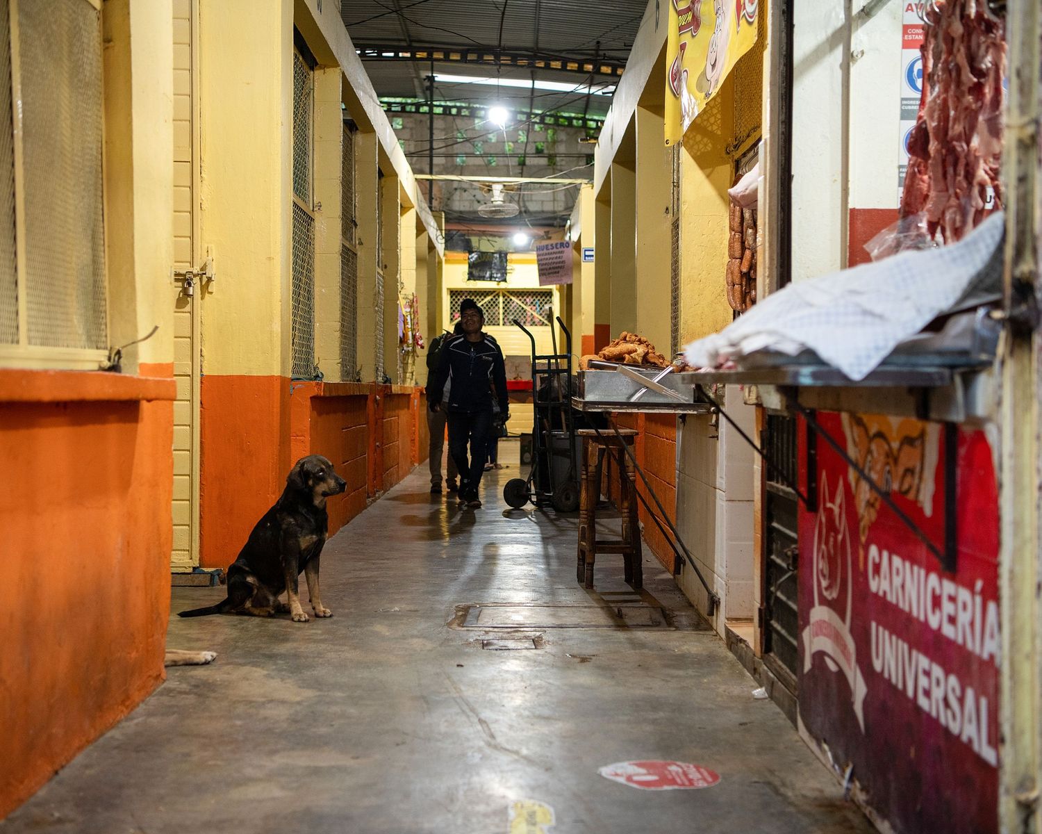 Long empty market corridor with orange and yellow walls and metal shutters.