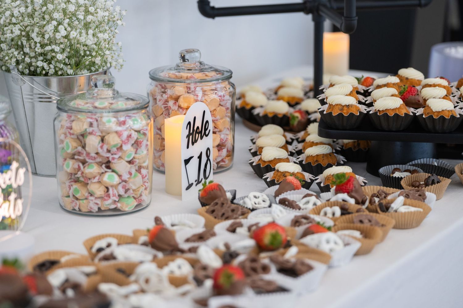 Elegant wedding dessert table with candy jars, chocolate treats, fruit tarts, and strawberry pastries displayed beautifully.