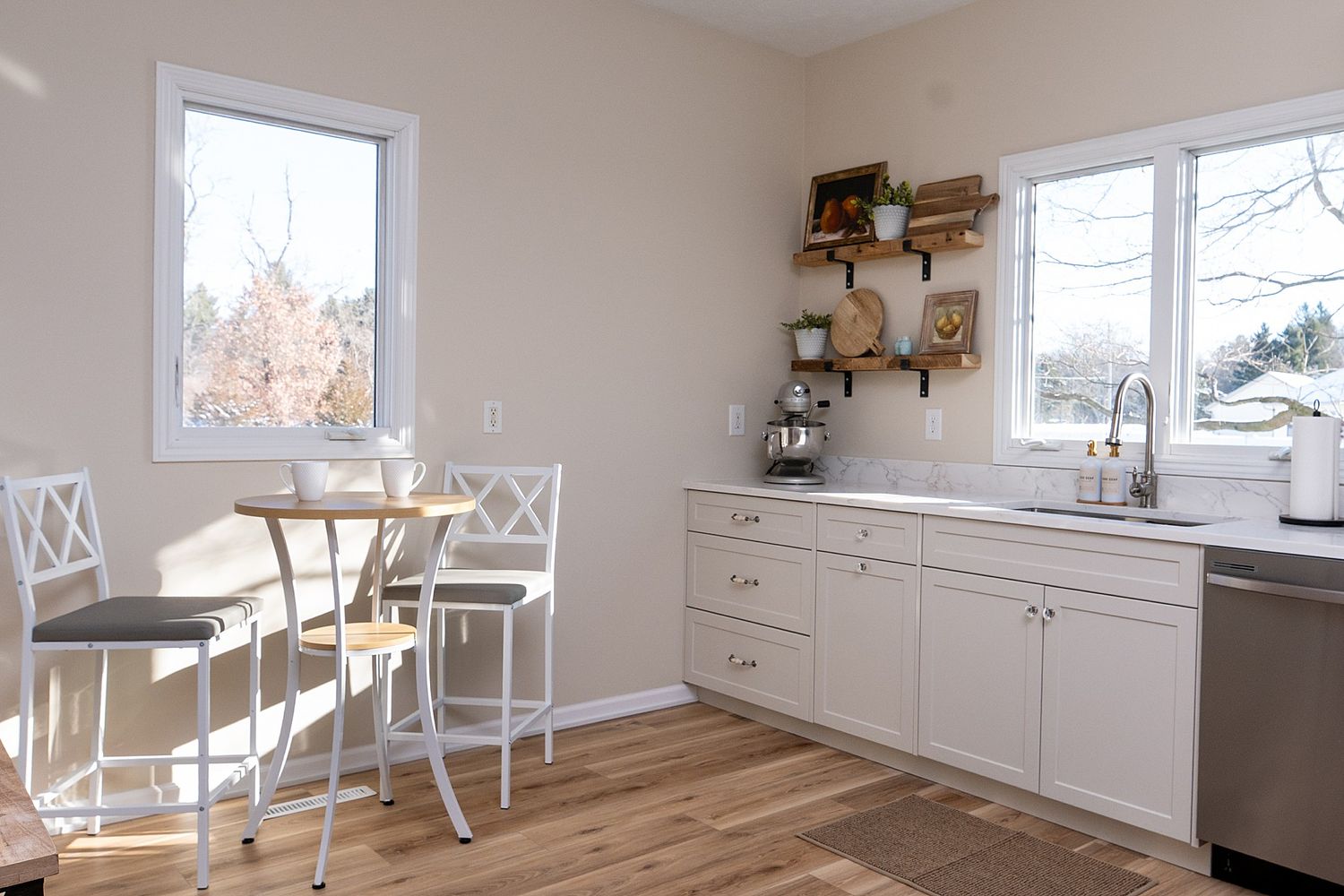 Bright kitchen with white cabinets, wood floors, dining set, open shelving, and dual windows allowing natural light.