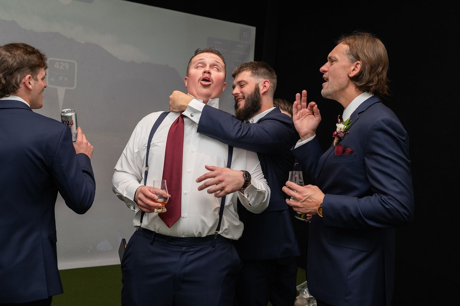 Groomsmen in navy suits celebrating and singing together at a wedding reception.
