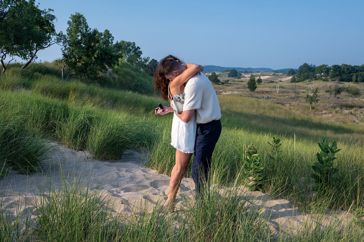 Scenic coastal landscape with sand dunes and tall grass against a blue sky.