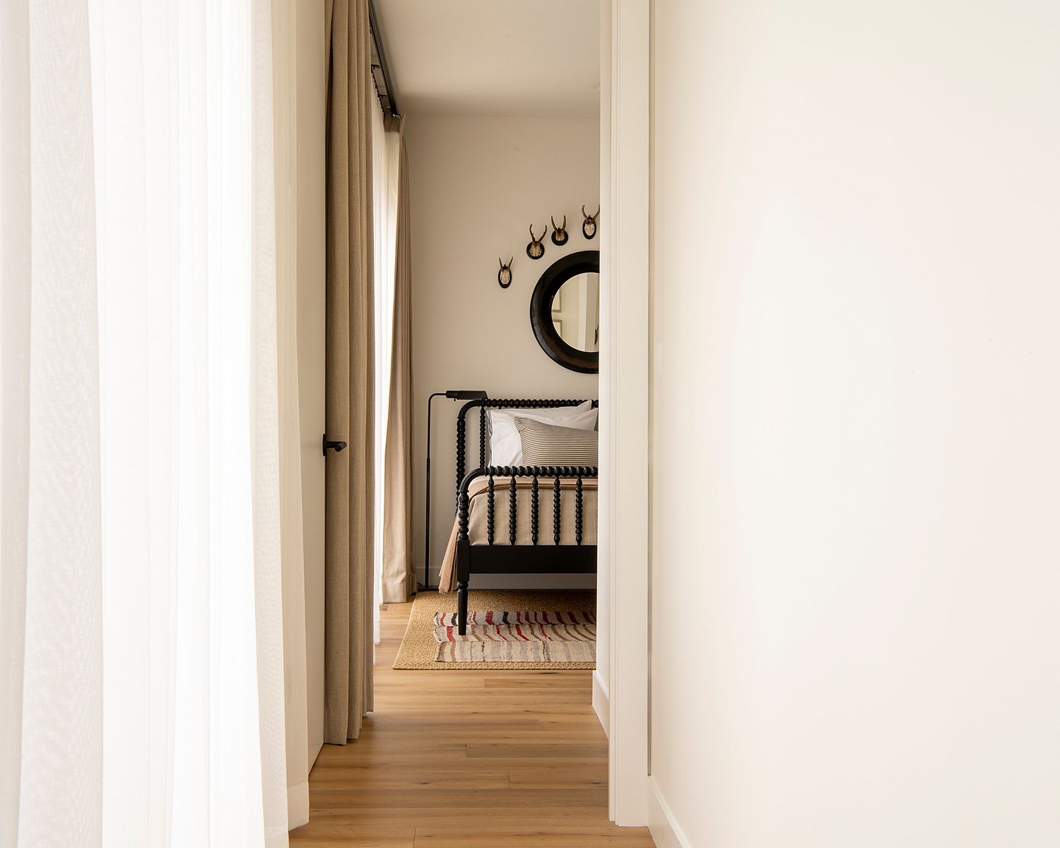 Minimalist hallway with wooden flooring and black circular wall decor leading to a bedroom.