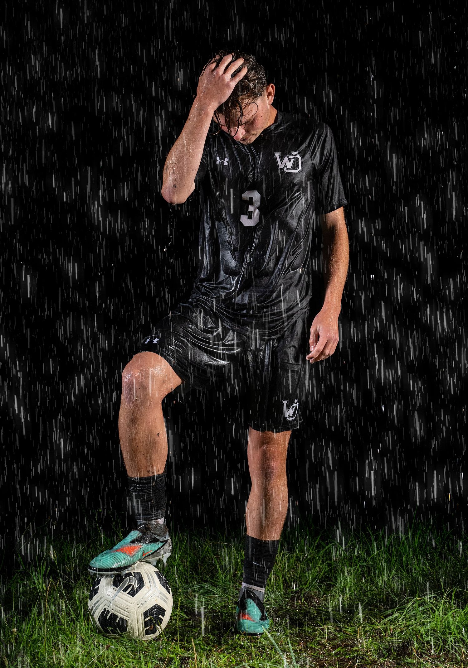 Soccer player practicing ball control drills in the rain on grass field.