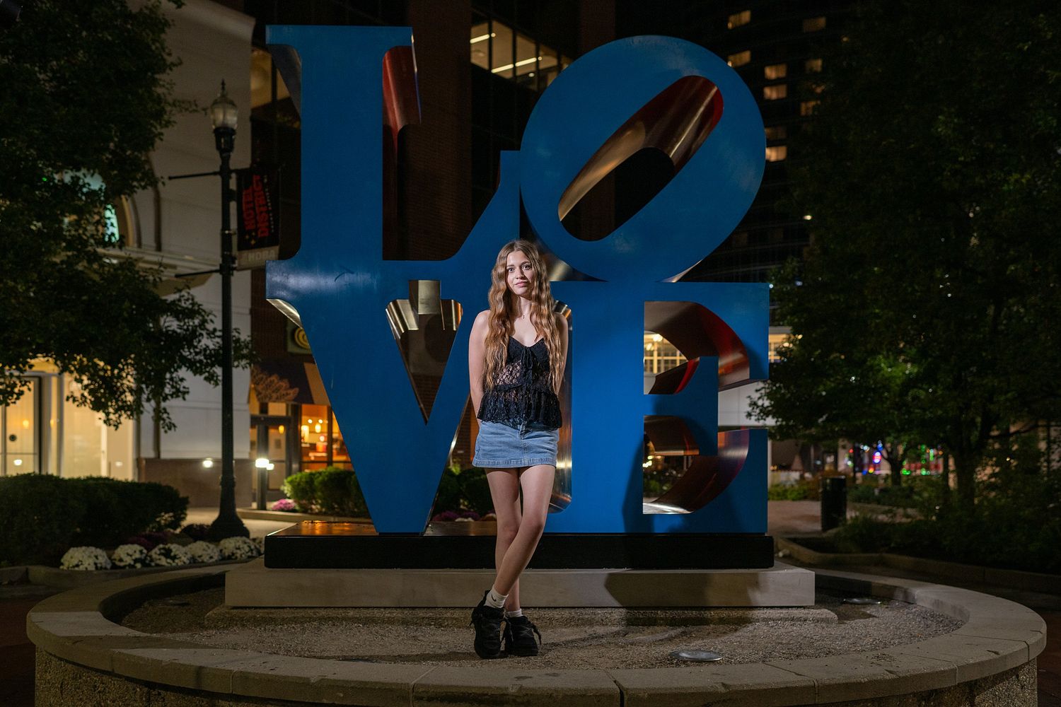 Urban plaza at dusk featuring a large blue sculptural art installation.