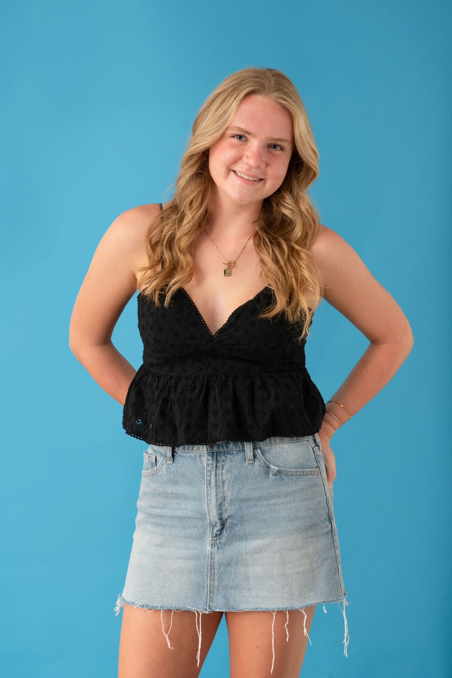Studio portrait against blue background wearing black top and denim skirt.