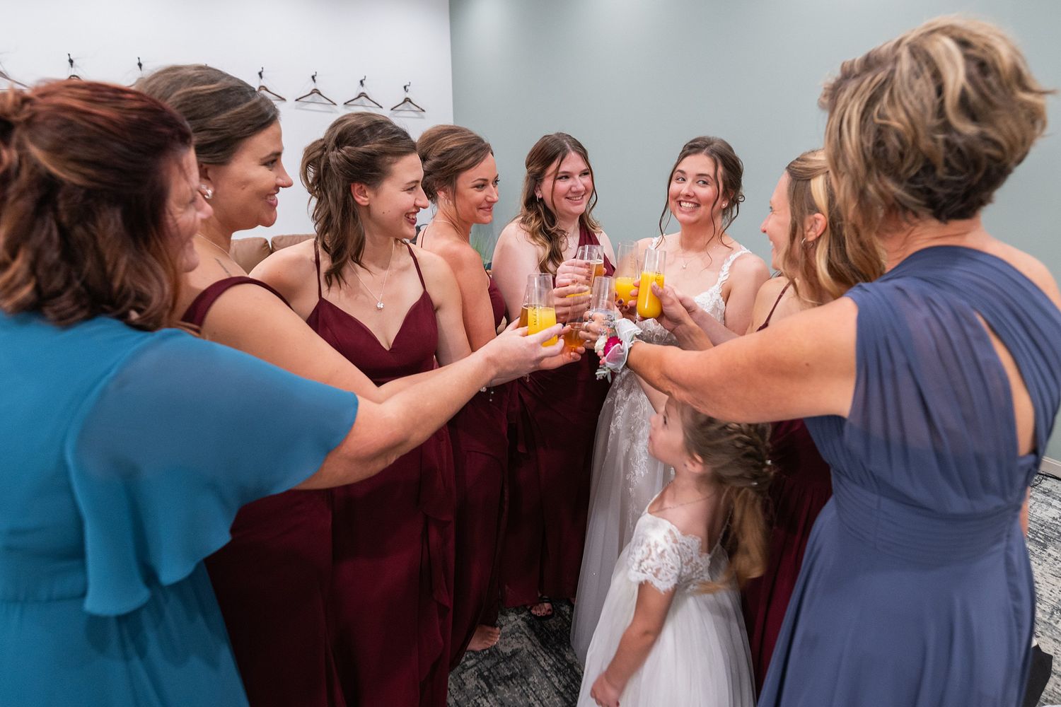 Bride and bridesmaids in burgundy dresses toasting with drinks before the wedding ceremony.