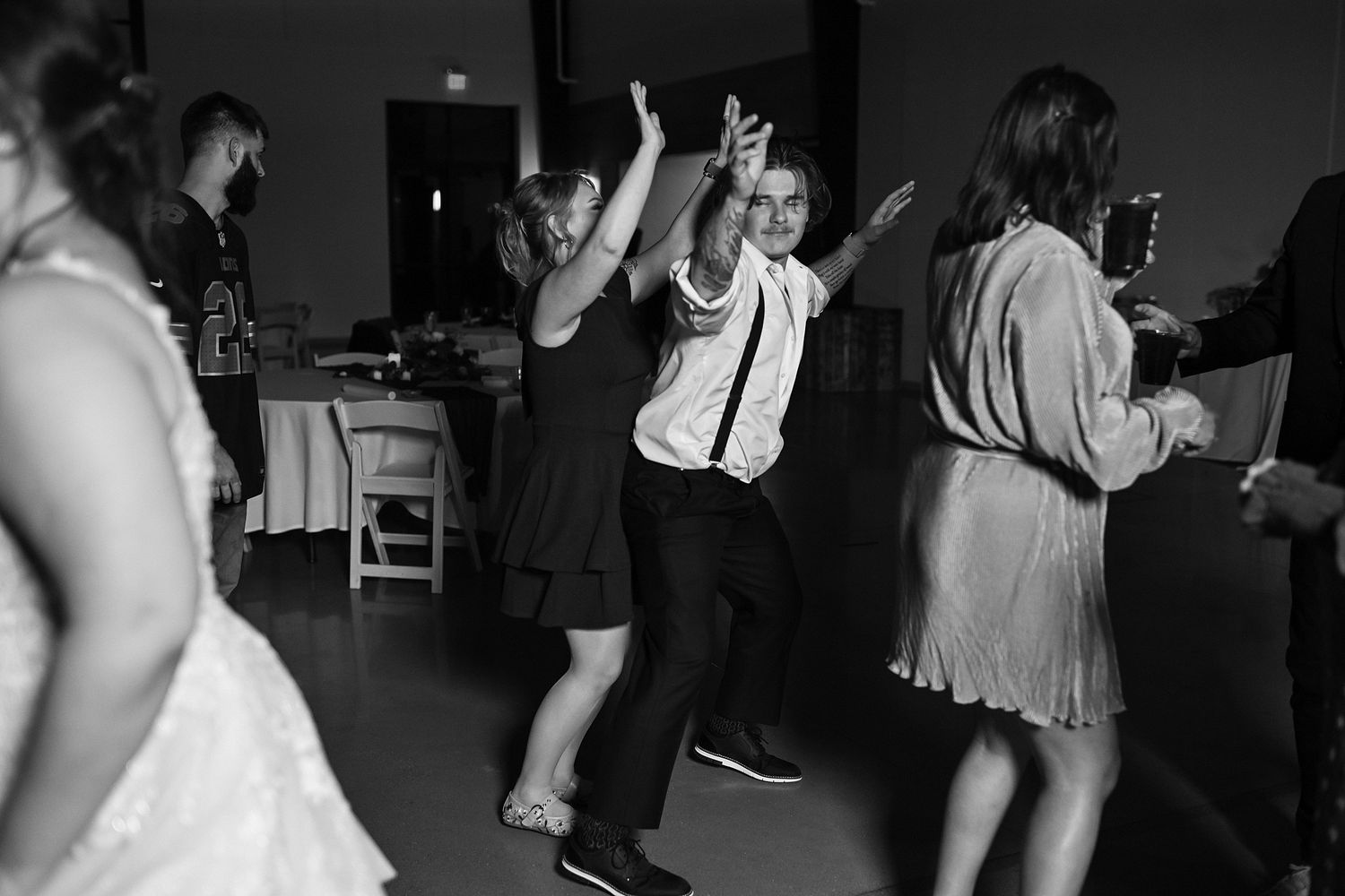 Wedding guests dance joyfully on the dance floor at a reception in black and white photo.