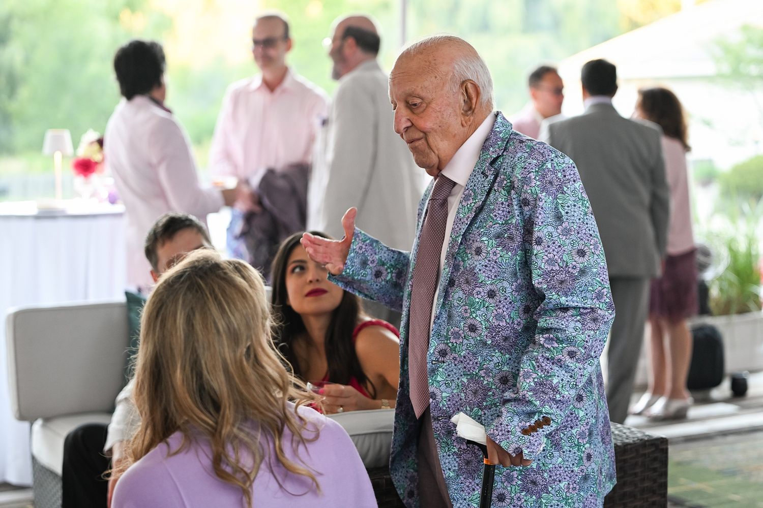 A person wearing a colorful floral blazer interacts with guests at an outdoor social gathering.