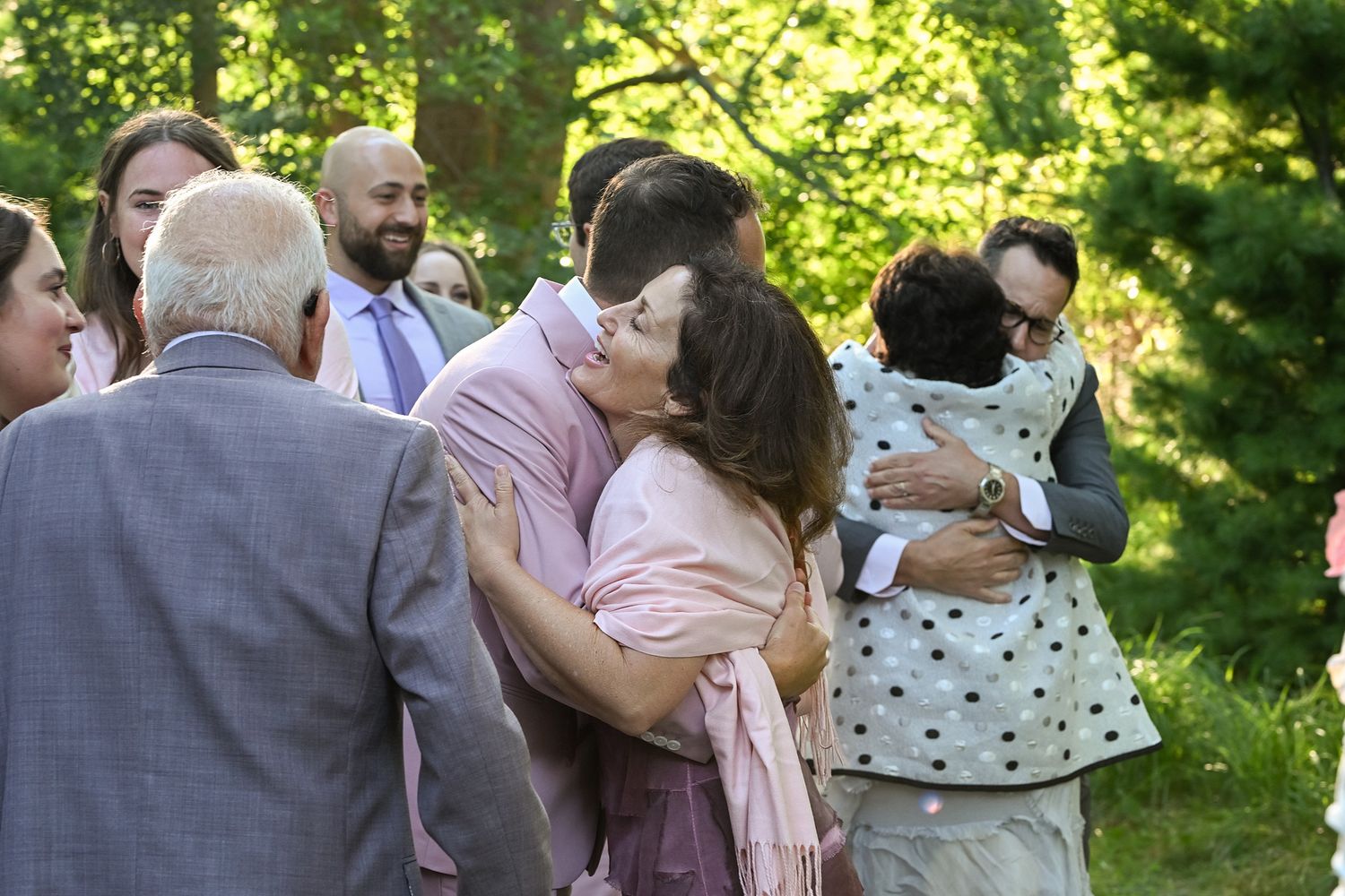 Wedding guests gather outdoors in a sunlit garden setting during a summer celebration.