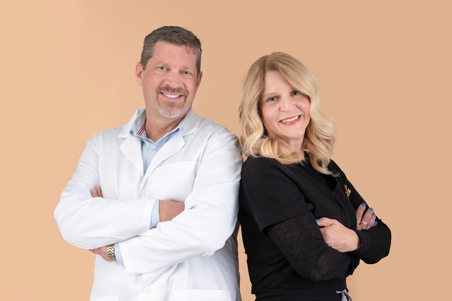 Two people posing together in professional attire against a peach colored backdrop.