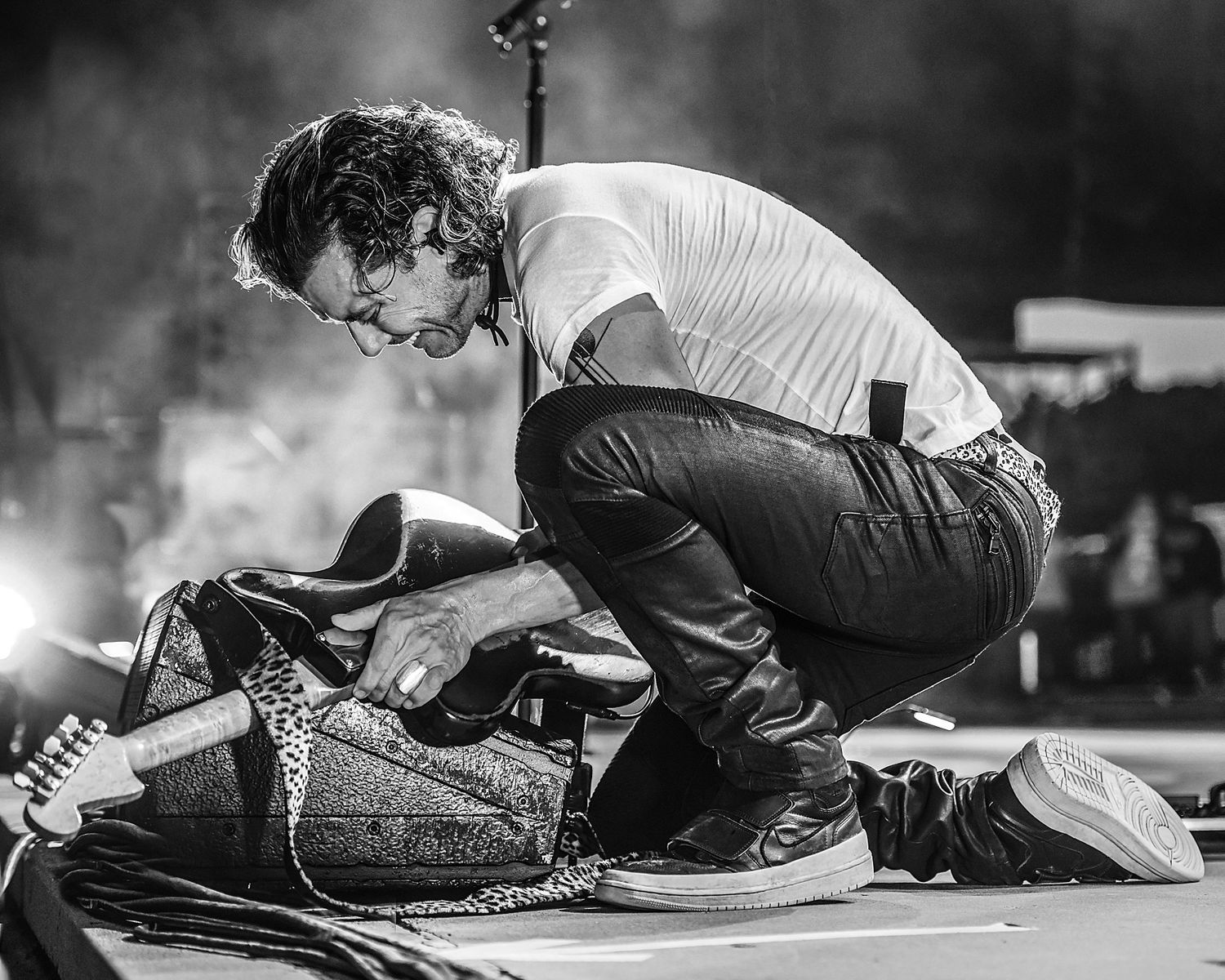 Dynamic black and white photo of performer crouching on stage with guitar.