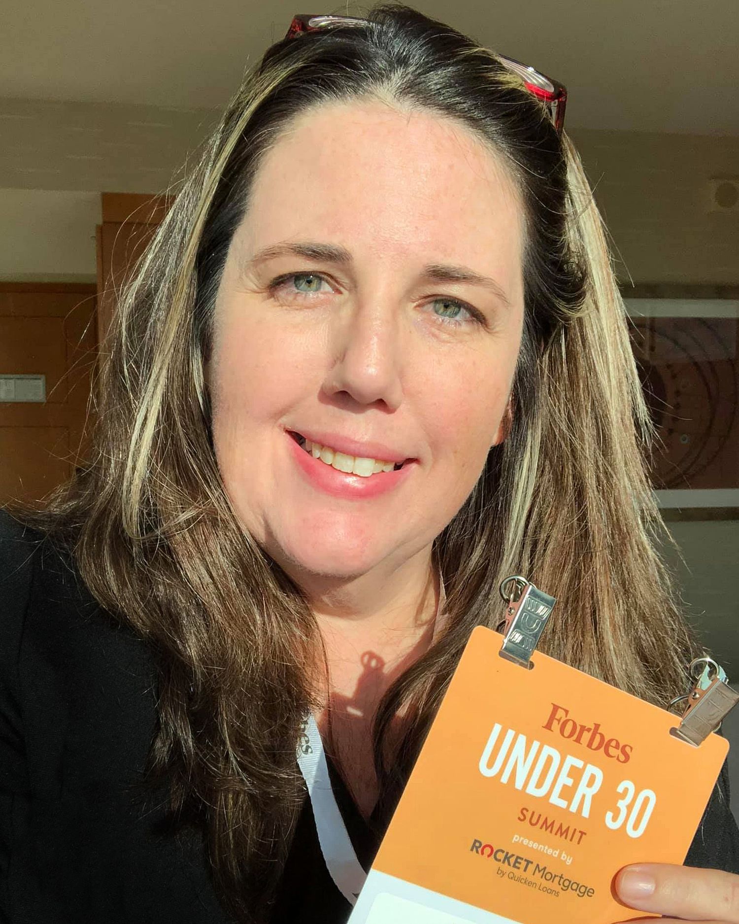 Person holding a Forbes Under 30 badge in an indoor setting.