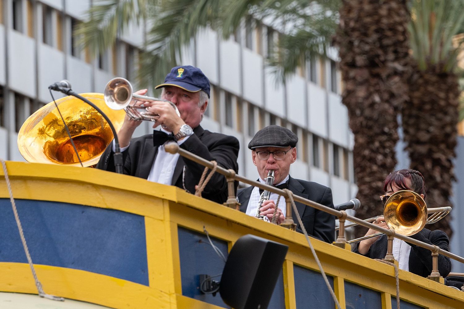 Musicians in dark attire perform on a yellow parade float during a carnival celebration.
