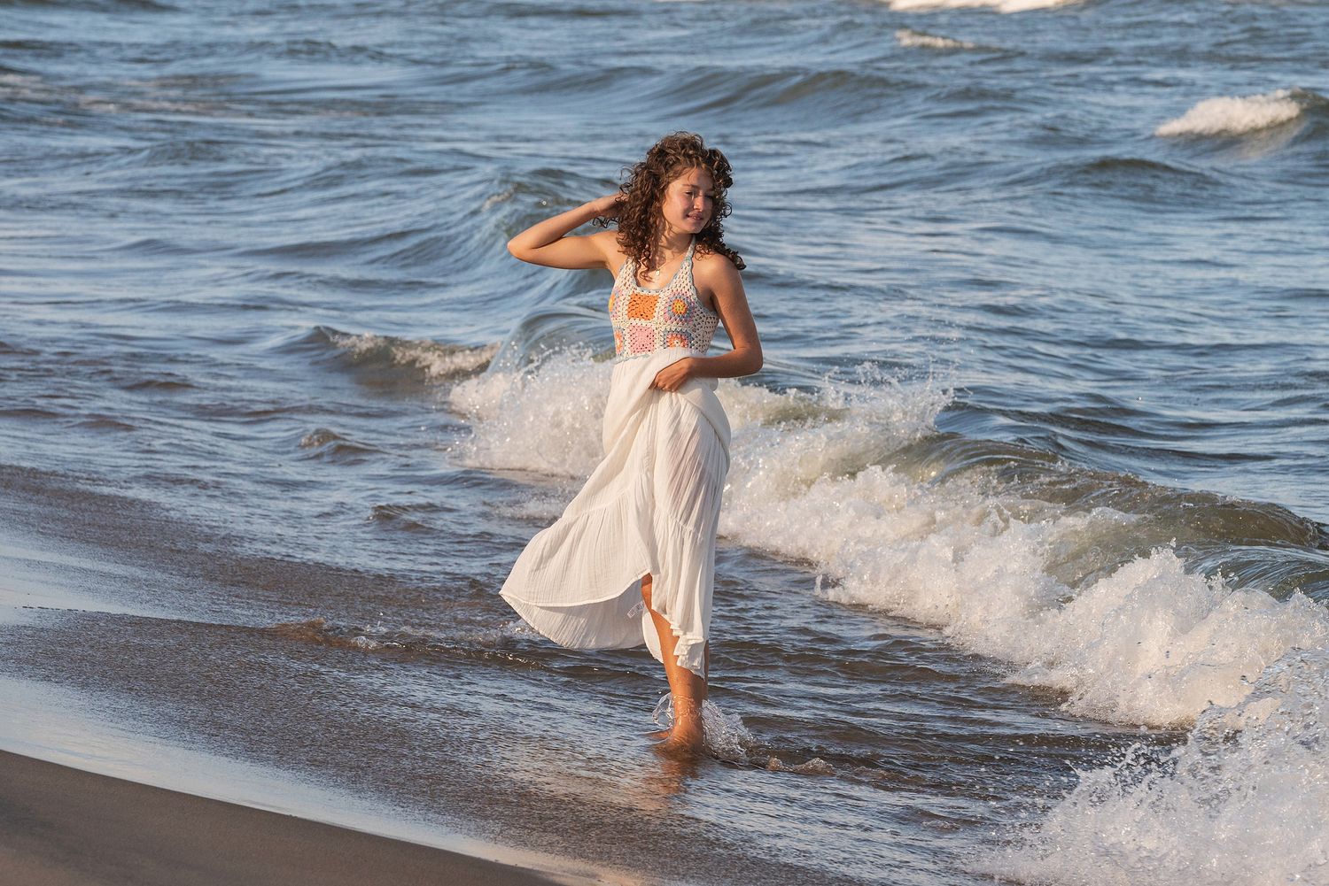 Someone in white plays in the ocean waves at the beach during golden hour.