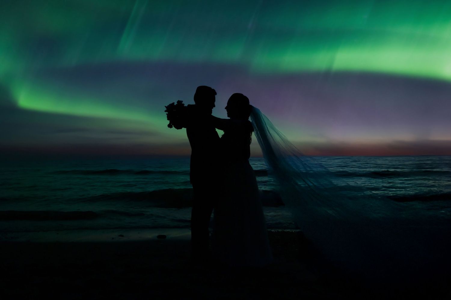 Silhouettes against a dramatic green aurora borealis in the night sky.