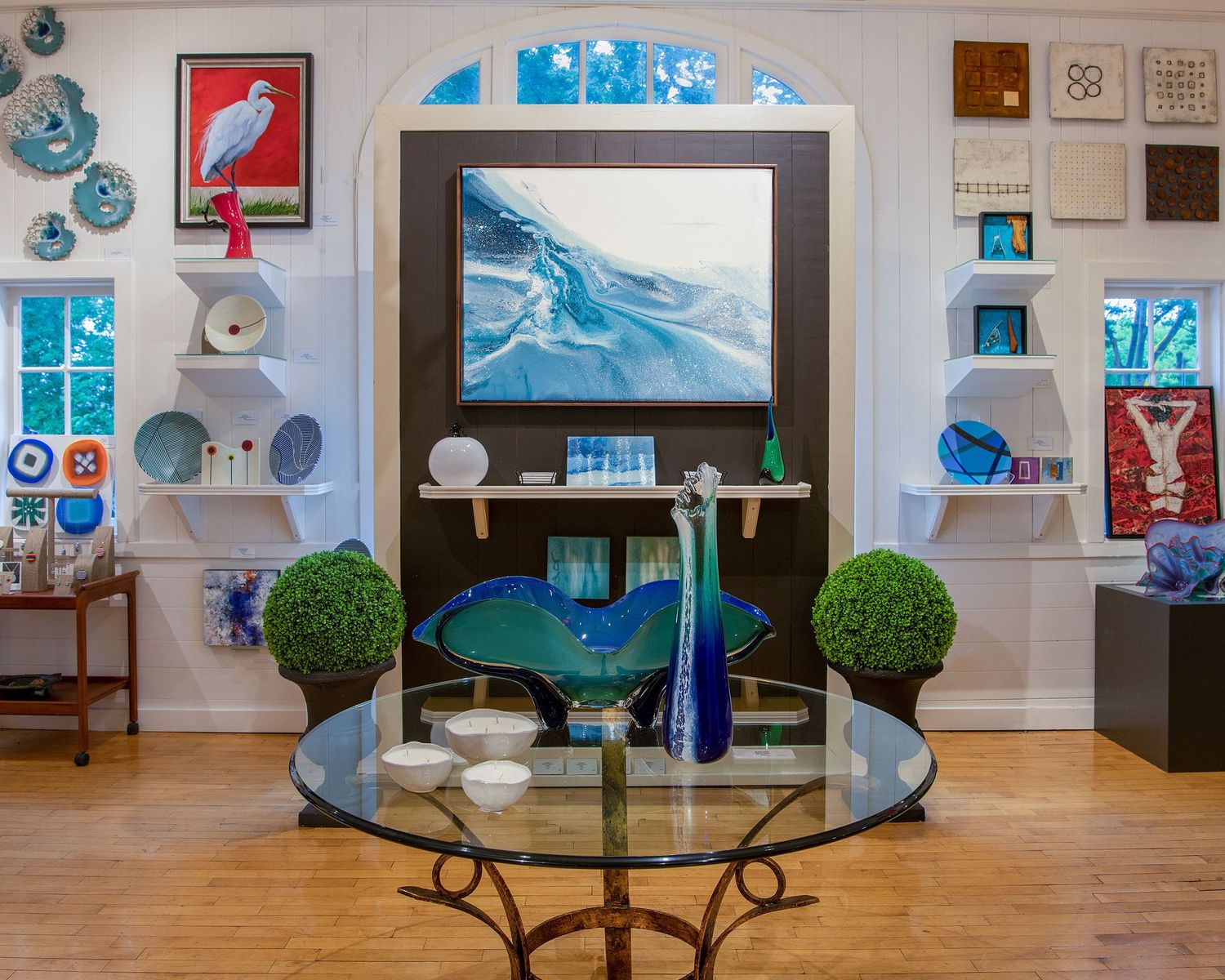 Modern living room with blue coastal decor, glass table and large abstract ocean artwork.