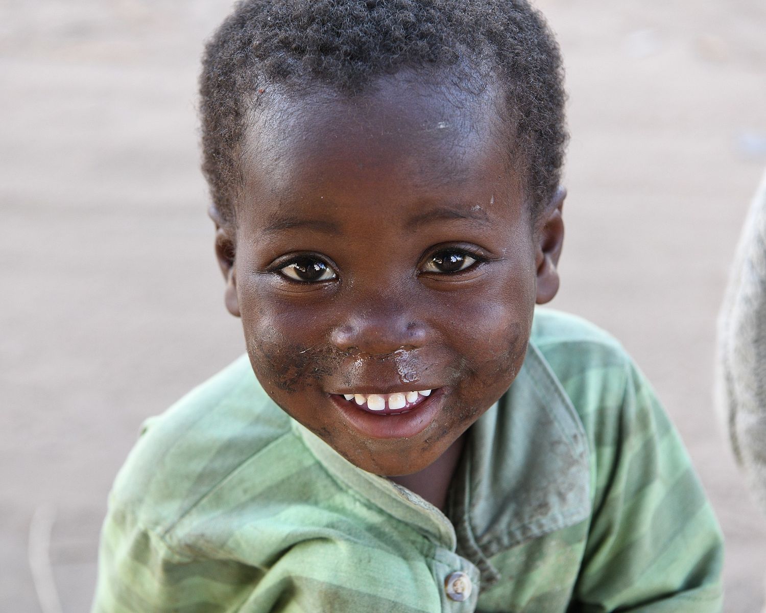 A young child wearing a light green hoodie smiles brightly at the camera.