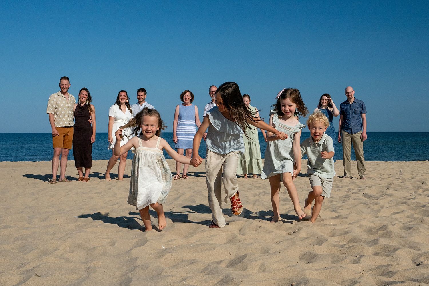 Family group portraits arranged along a sandy beach with ocean and blue sky in background.