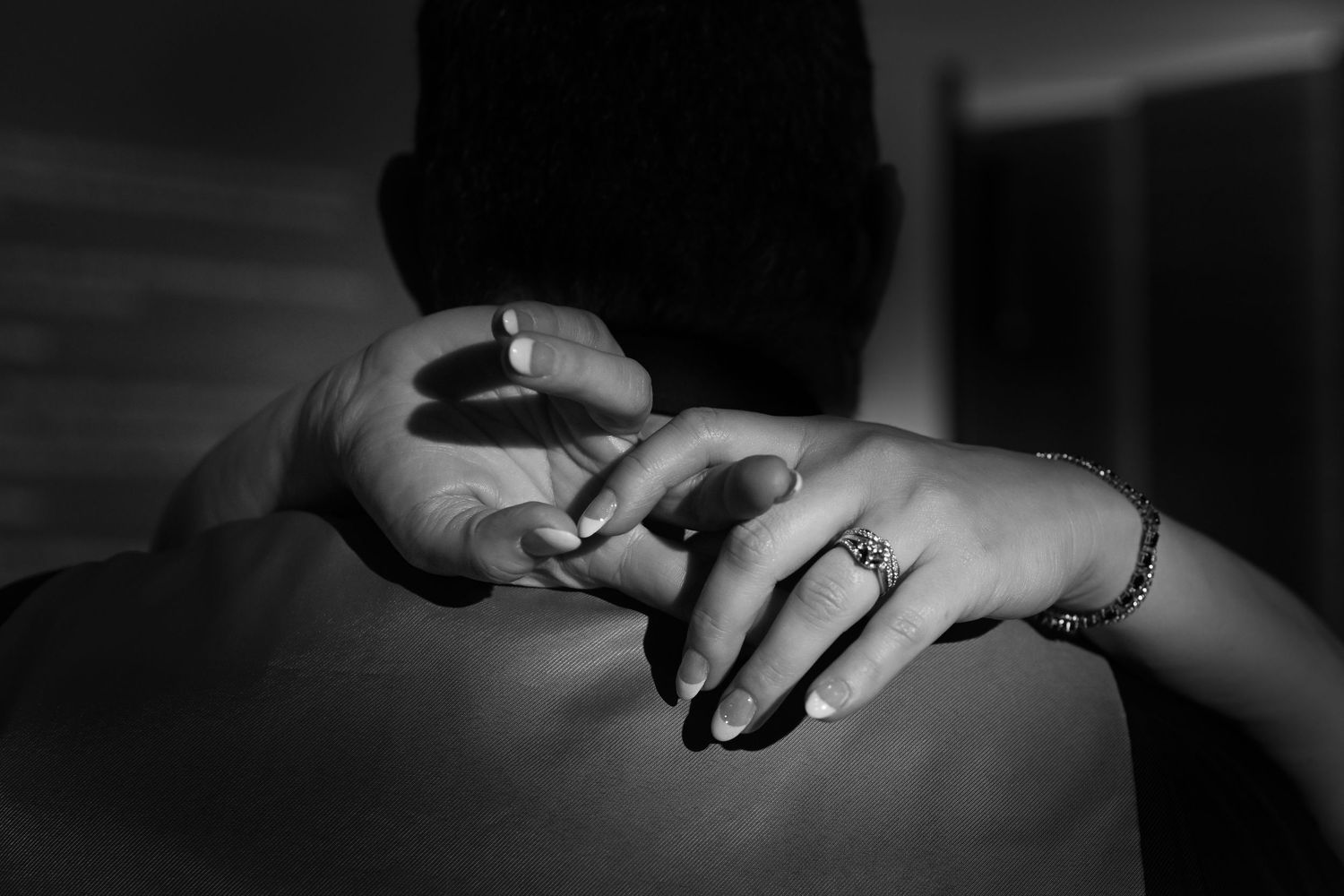 Black and white photo of hands with a ring and bracelet touching someone's bare back.