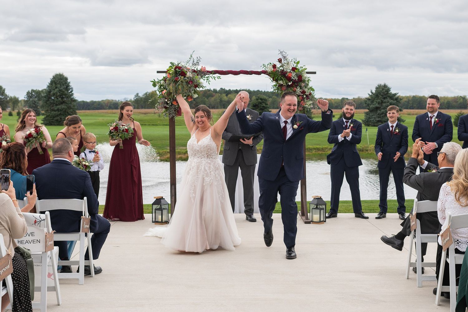 Newlyweds celebrate with raised hands walking back down aisle after outdoor wedding ceremony.