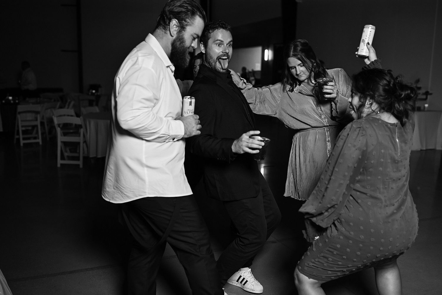 Wedding guests laugh and dance together in black and white photo at reception.