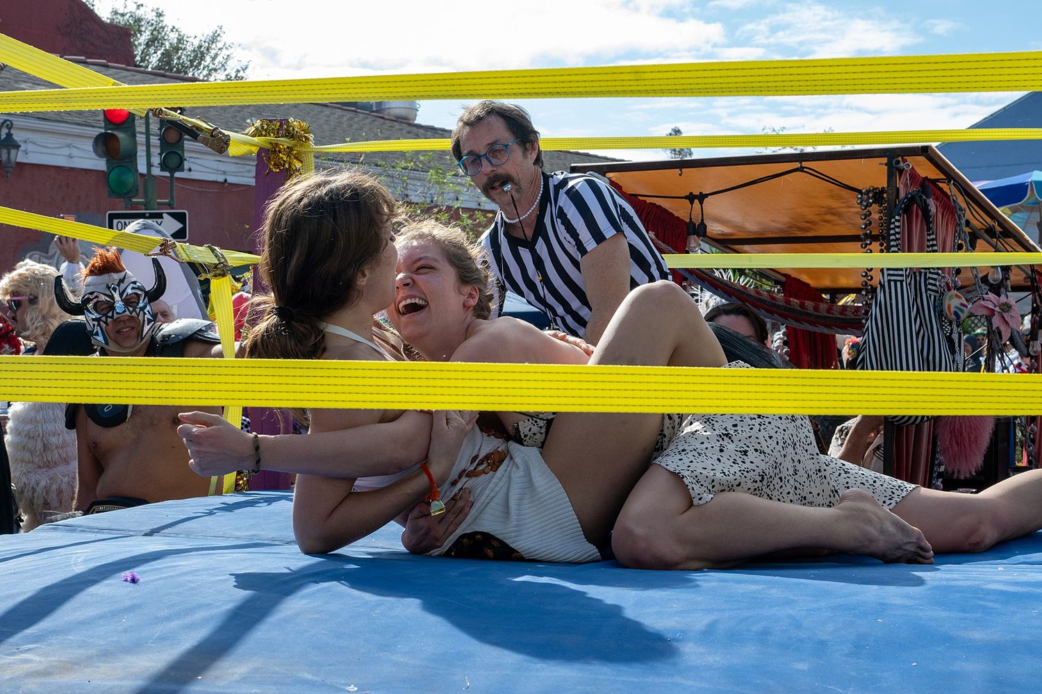 Wrestling performance taking place on a blue mat with yellow ropes during an outdoor event.
