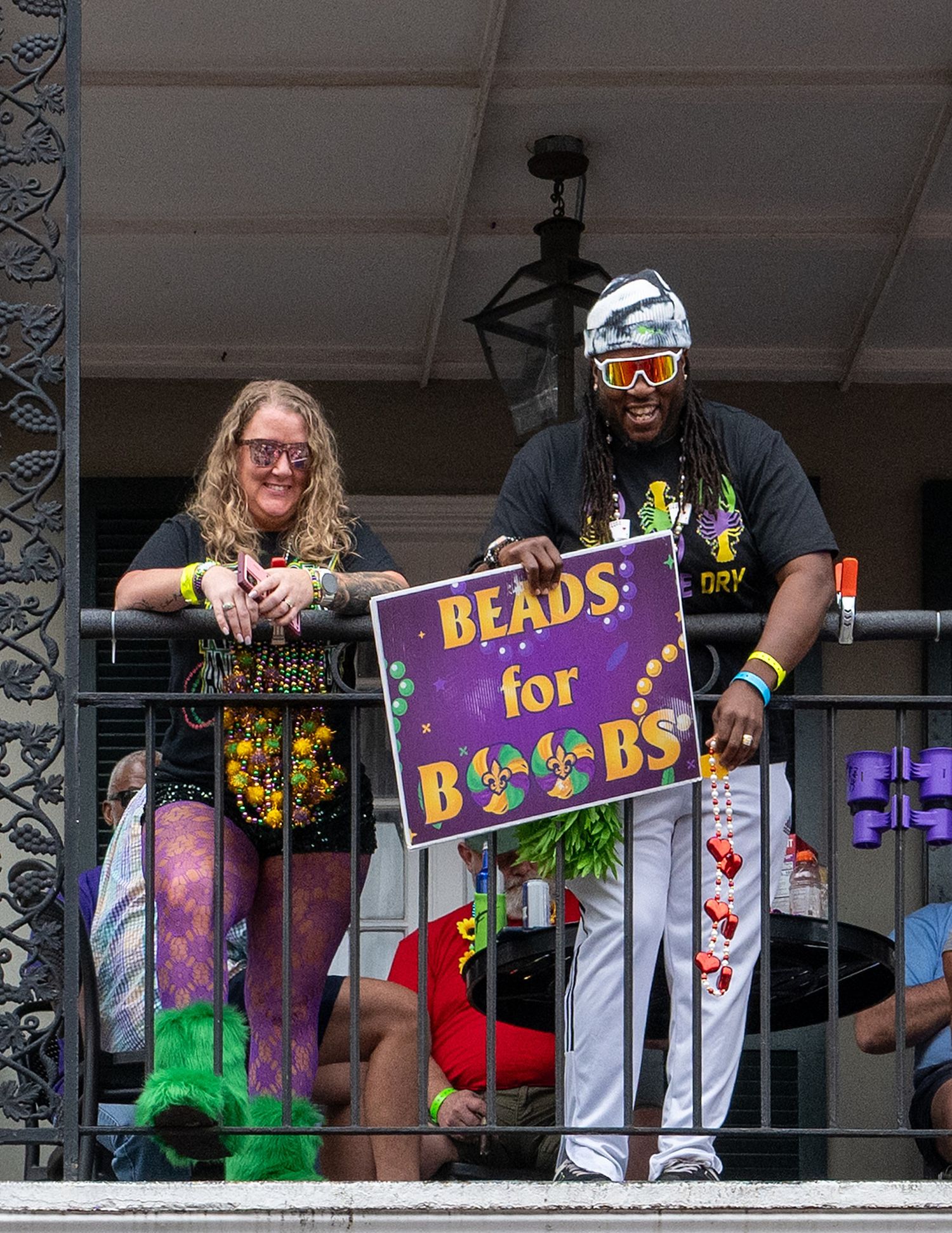 People holding beads signs on a balcony decorated with purple and green banners.