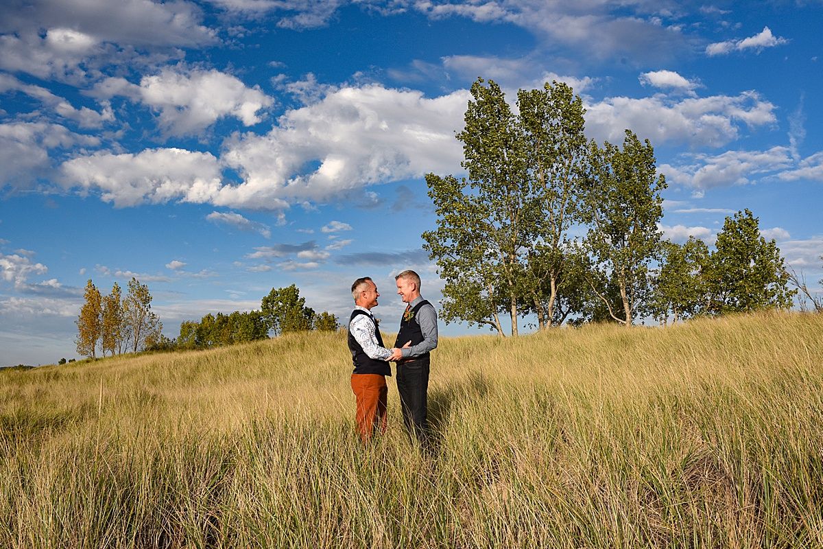 Wedding portraits taken in golden field under bright blue sky with scattered clouds.