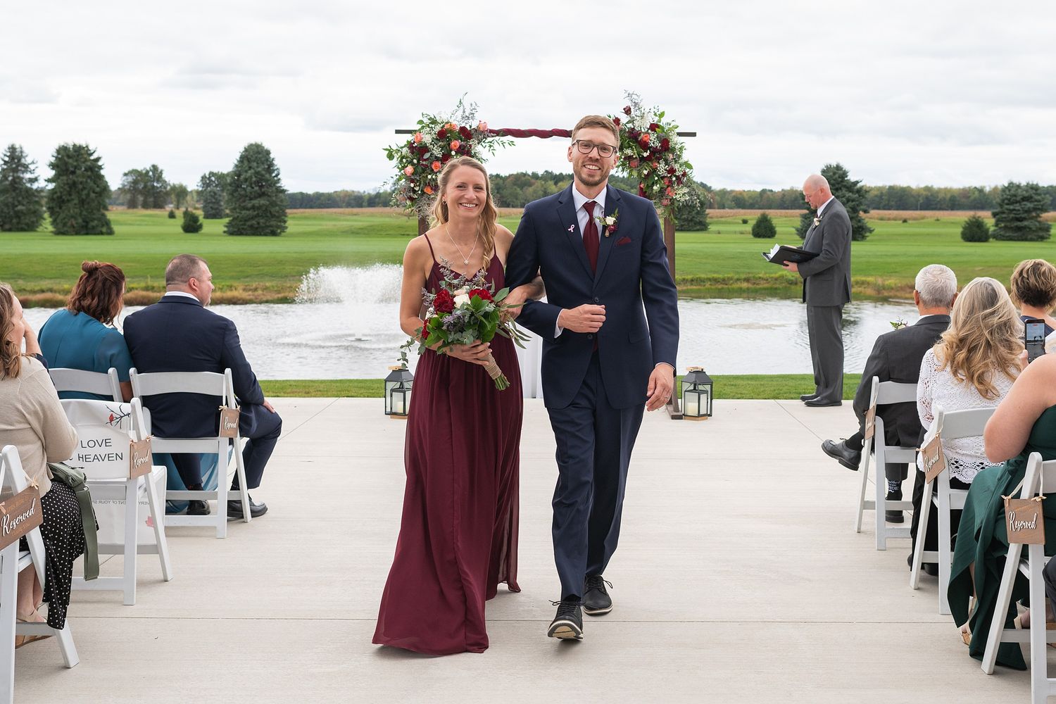 A bridesmaid in burgundy and groomsman in navy walk down the aisle after the wedding ceremony.