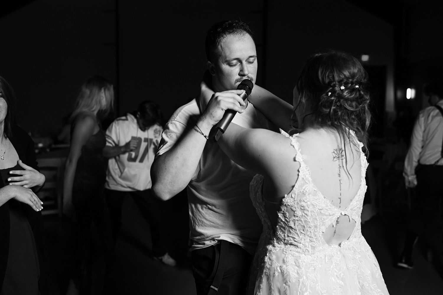 Black and white photo of bride and guest dancing closely at lively wedding reception.