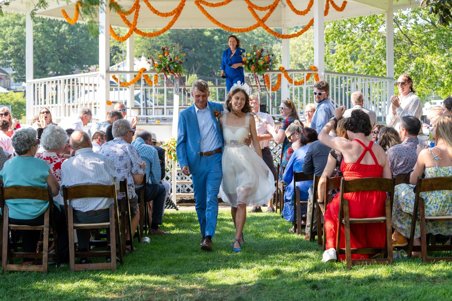 Outdoor wedding reception with orange decorations and guests seated at tables under a tent.