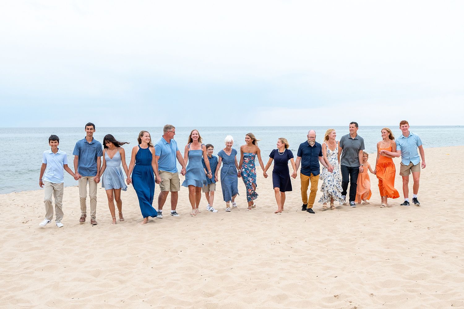 Large family group poses together on beach wearing coordinated blue and white outfits.