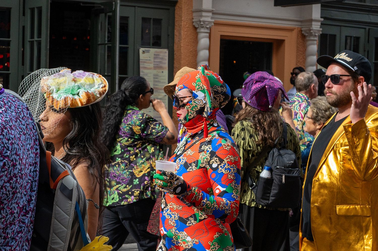 Colorfully dressed partygoers celebrate beneath decorated balconies in New Orleans French Quarter.