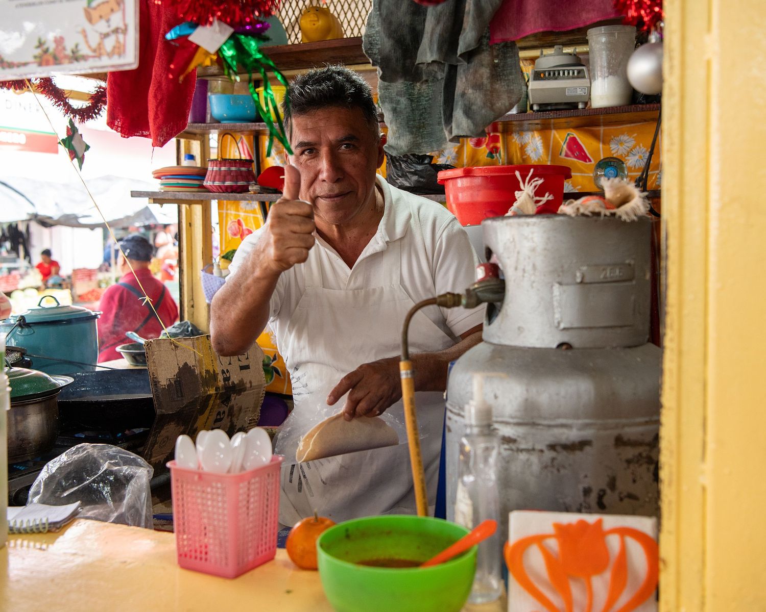 Colorful food stalls with vendors serving customers at an outdoor market.