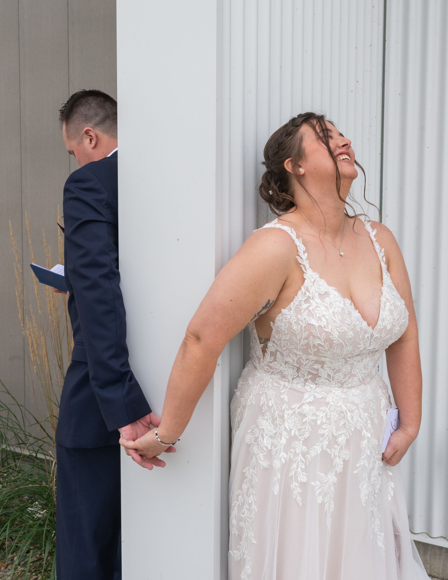 Bride and groom share an emotional first look moment, holding hands around a corner before their wedding ceremony.