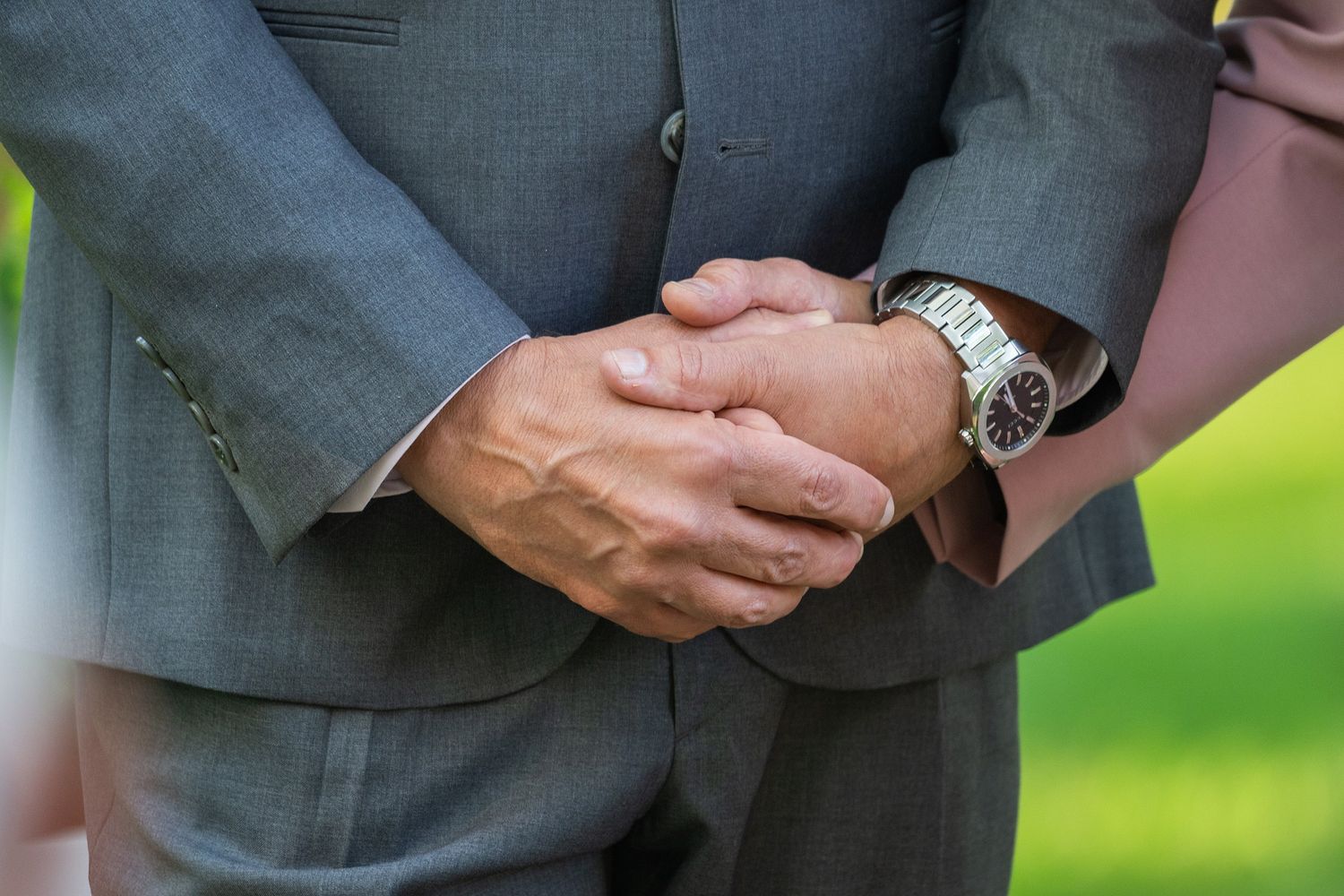 Close-up view of hands exchanging wedding rings during an outdoor ceremony with green background.