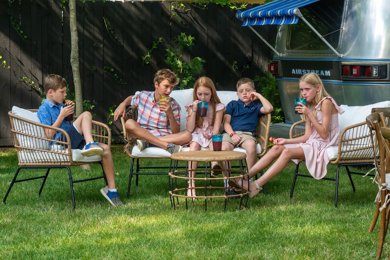A group relaxes together on outdoor patio furniture on a sunny lawn during a casual summer gathering.