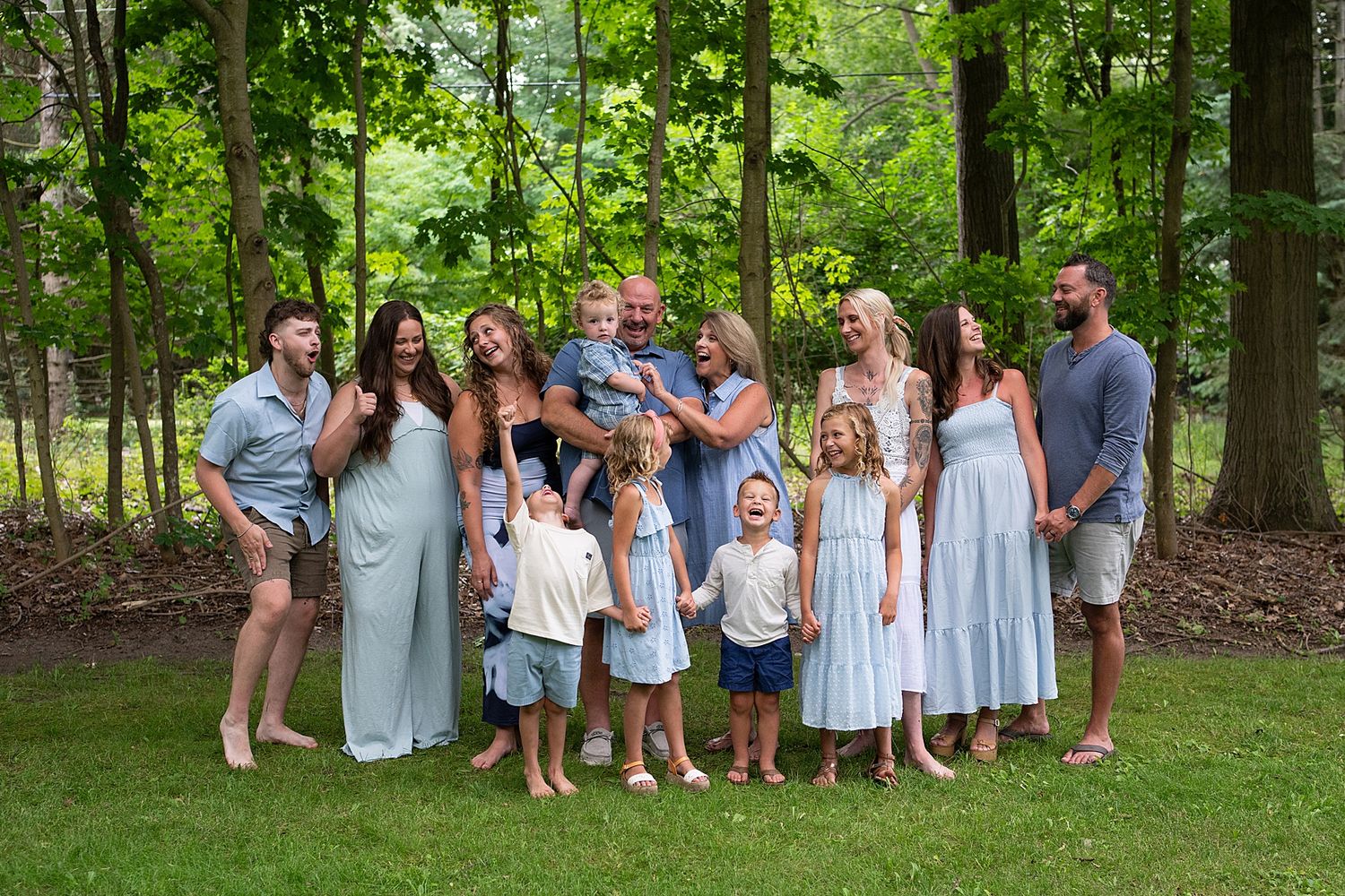 Large family group in coordinated blue and white outfits posed in wooded setting.