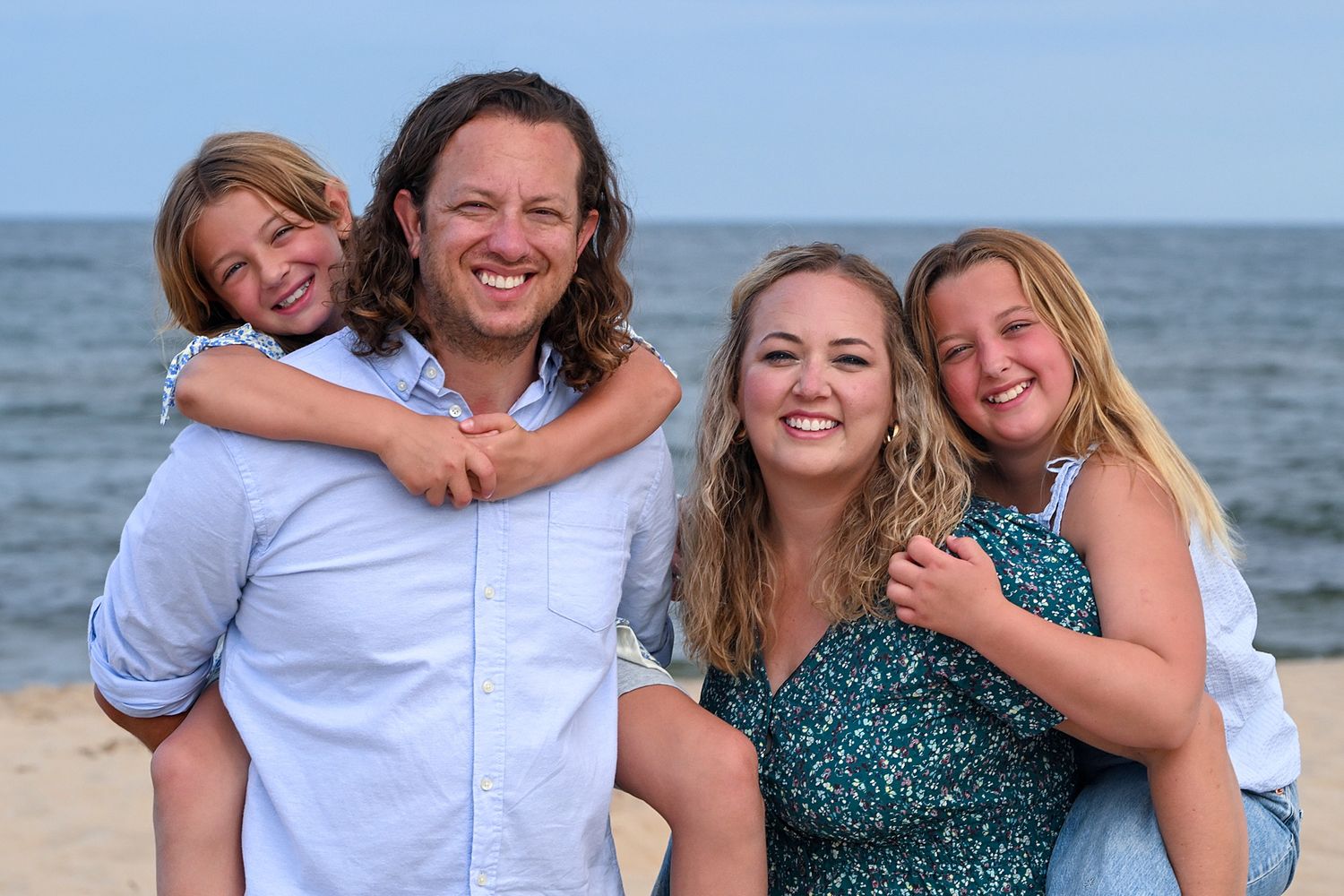 Casual family beach portraits with coordinated outfits against an ocean backdrop.