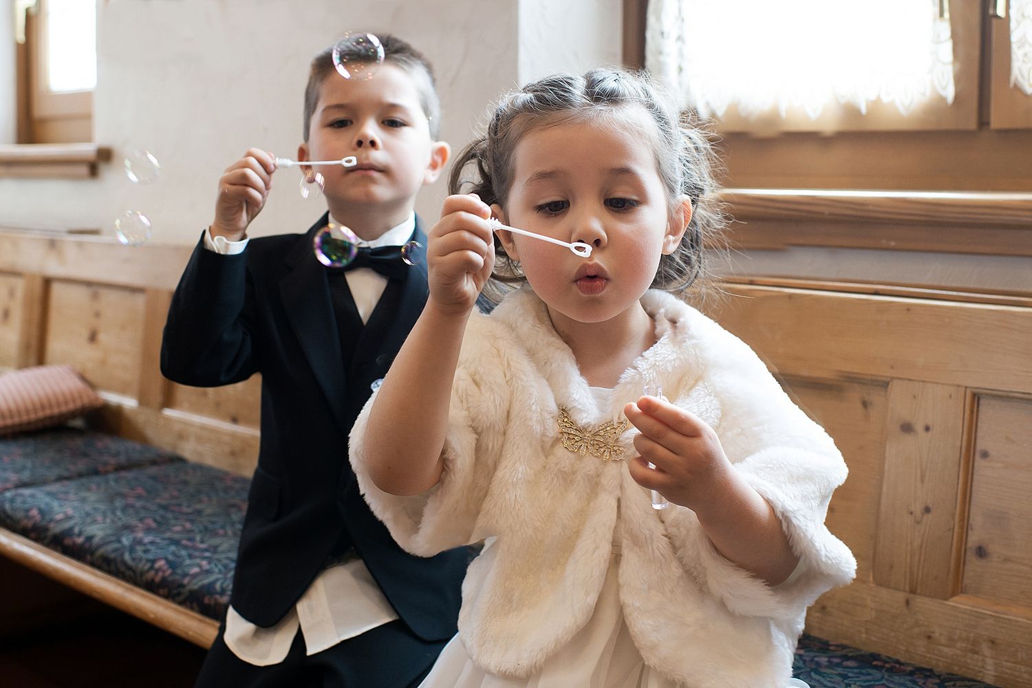 Young children in formal attire blowing bubbles at a wedding celebration.